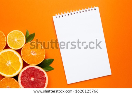 Notebook and citruses fruits on orange background, fruit flatlay, summer minimal compositon with grapefruit, lemon, mandarin and orange. Summer color , harvest, cutting fruits