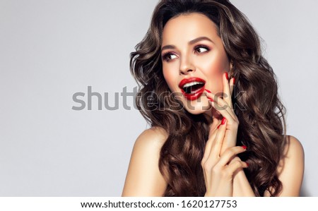 Beautiful laughing brunette model  girl  with long curly  hair . Smiling  woman hairstyle wavy curls . Red  lips and  nails manicure . Fashion , beauty and make up . Expressive facial expressions
