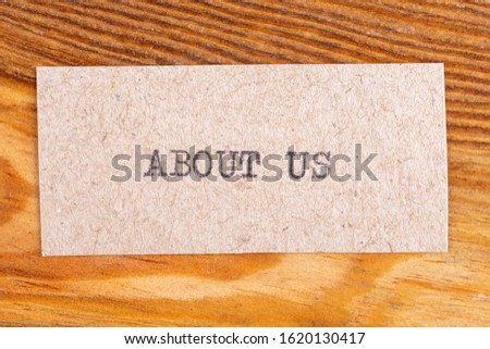 The word "about us" typed. The inscription on a gray sheet of pappier. Wood texture background.