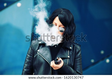 stylish girl smoking an e-cigarette as she is walking through the city. young woman smoking electronic cigarette