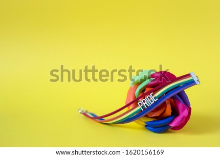 On an artificial rainbow rose lies a rainbow bracelet with the inscription Pride, on a yellow background. LGBT concept