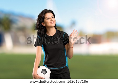 Young football player woman saluting with hand with happy expression at outdoors