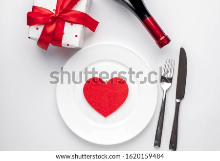 
Table setting for Valentine's Day - white plate, wine, gift, kitchen appliances, hearts on a white background