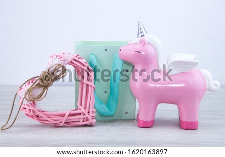 A pink unicorn stands next to a gift bag and a toy heart. Cute gift for a girl.