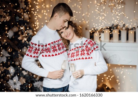 Loving couple. Happy couple in love holding glass of champagne, posing. Valentines day. Stylish couple, guy and girl in sweaters with hearts. Girl with beautiful makeup and afro curls