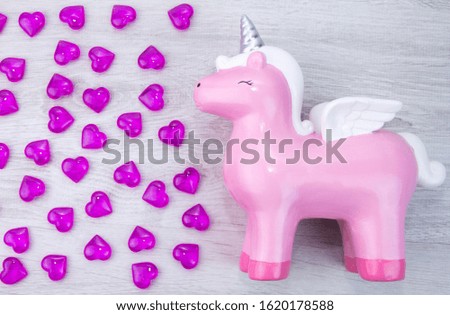 Cute pink unicorn on a wooden background. Lots of hearts. Valentine's day.