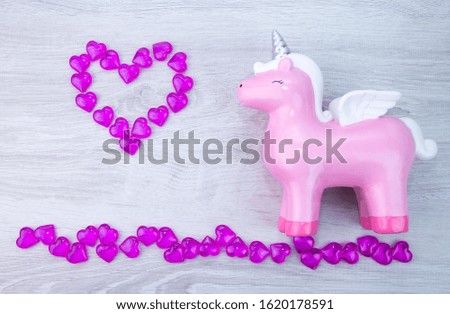 Cute pink unicorn on a wooden background. Lots of hearts. Valentine's day.