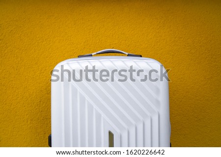 White travel bag on a yellow wall background.