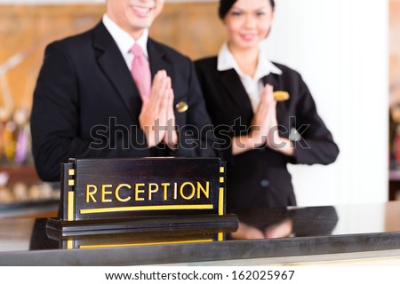 Chinese Asian reception team at luxury hotel front desk welcoming guests with typical gesture, a sign of good service and hospitality