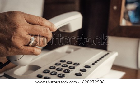 Closeup of female hand holding telephone receiver and dialing a phone on a classical white telephone. Royalty-Free Stock Photo #1620272506