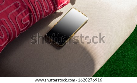 cell phone half in the sun, on cavas chair, with green grass, with red pillow