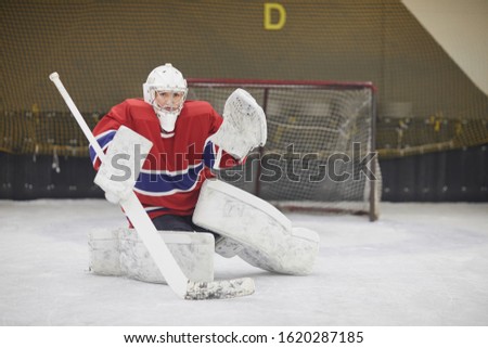 Full length portrait of female hockey player in full gear looking at camera while defending gate during match, copy space