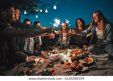 Happy friends having fun with fire sparkles. Young people camping at picnic on the night. Youth friendship concept on night mood