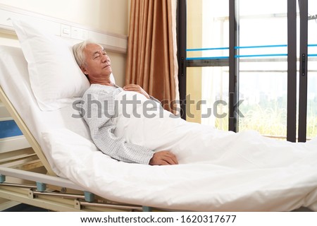 asian elderly male patient lying in bed sleeping in hospital ward or assisted living facility