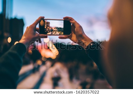 Selective focus on modern cellular phone using for clicking pictures via camera, millennial woman tourist taking photos or shooting video via mobile phone during evening walk for exploring new city