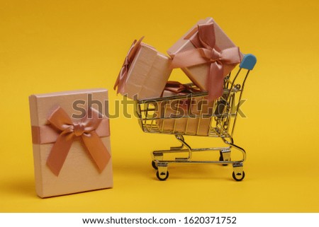 Shopping trolley and gift boxes with bows on yellow background. Composition for christmas, birthday or wedding.
