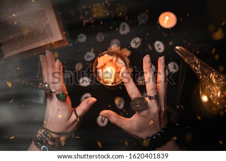 Astrology and esotericism. Female witch hands conjure over a candle. On a black background lie fortune-telling runes, a book, precious amulets, a copper lamp and a candle. Dark magic. Royalty-Free Stock Photo #1620401839