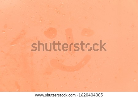 The picture or figure of the smiling face on the orange or pink evening or morning window glass with drops 