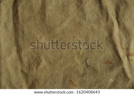 Old, crumpled and dirty khaki color tarpaulin, detailed texture. Fabric of a vintage army military or travel backpack for background. Worn natural sail cloth material with stains Royalty-Free Stock Photo #1620408643