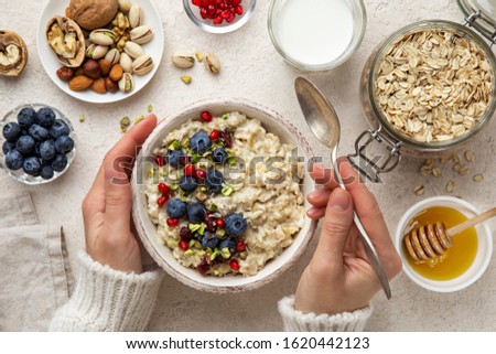 healthy breakfast. Woman eating oatmeal porridge with fresh berry, nuts and honey, top view Royalty-Free Stock Photo #1620442123