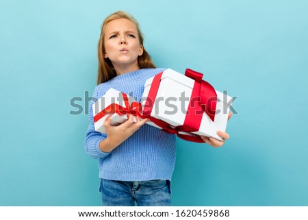 Portrait of little caucasian girl with long brow hair in blue hoody holds a white boxes with gifts isolated on blue background