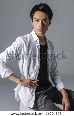 Casual young man sitting on a cube on gray background
