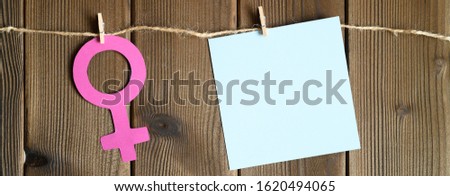 female symbol cut out of paper and blank sticky note attached with a clothespin to a rope on a wooden background. the concept of gender equality. space for text