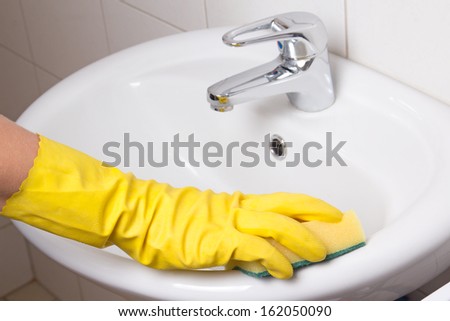 Hand in yellow glove with sponge cleaning white sink