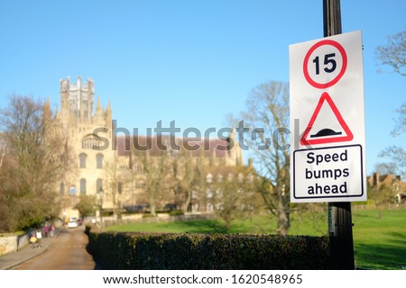 Shallow focus of a general speed limit and speed bump sign located nearby a large cathedral. Traffic calming measures are in place in the area.
