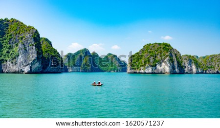 two unidentified people wearing traditional Vietnamese hats are on a boat in the sea around the area of Halong bay d of Vietnam with a background of colourful blue water, sky and lush rocky mountains Royalty-Free Stock Photo #1620571237