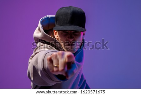 Men portrait in a neon light. Beneath in the hoodie and hat. Dark face. Hip-hop style.