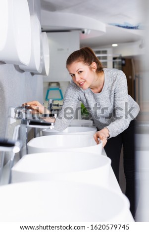 Smiling female buyer choosing ceramic washbasin in bathroom fitment shop