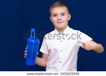 Cheerful young  caucasian schoolboy with white shirt and blue sports bottle.Boy shows to drink bottle.Dark blue background.