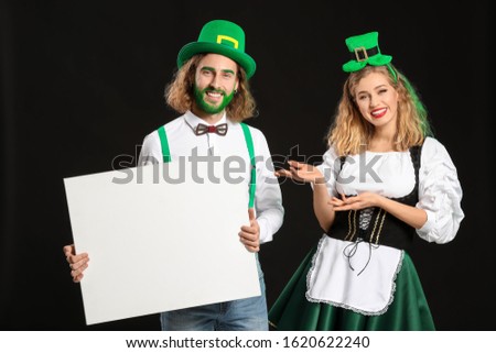 Young couple with blank poster on dark background. St. Patrick's Day celebration