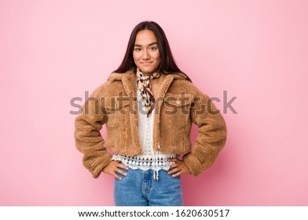 Young mixed race indian woman wearing a short sheepskin coatconfident keeping hands on hips.