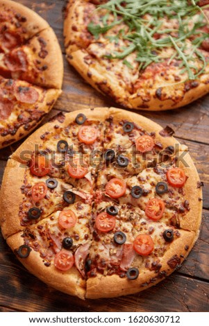 Composition of three various kinds pizzas placed on rusty scratched wooden table. Hot and fresh food ready to eat