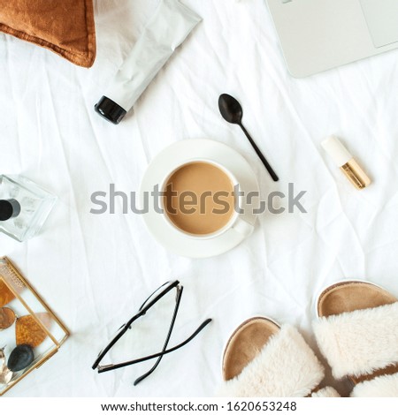 Morning breakfast with coffee in bed with white linen. Flat lay women fashion, beauty background with laptop, cosmetics, accessories. Slippers, concealer, earrings, perfume. Top view.