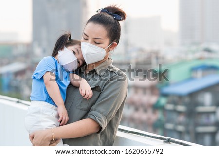Asian mother and little young daughter wearing mask for prevent dusk pm 2.5 bad air pollution on deck in Bangkok city Thailand 2020.  Royalty-Free Stock Photo #1620655792