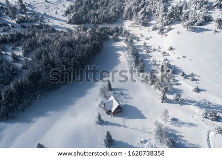 Aerial view of a mountain house covered in snow on a sunny winter morning