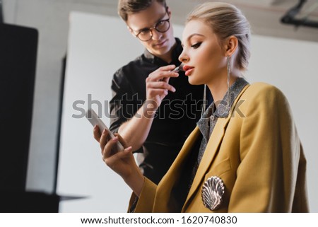 low angle view of Makeup Artist doing makeup to stylish model with smartphone on backstage