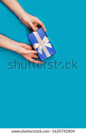 Gift box with surprise in a female hands on blue background. Flat lay, top view, place for text.