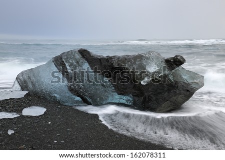 Ice block on a beach with lava stones and water floating over.
