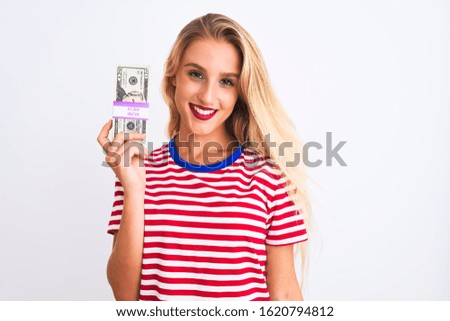 Beautiful woman wearing red striped t-shirt holding dollars over isolated white background with a happy face standing and smiling with a confident smile showing teeth