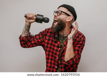Karaoke concept. Young, happy hipster man with beard singing a song with a microphone. Guy in black hat and eyeglasses.