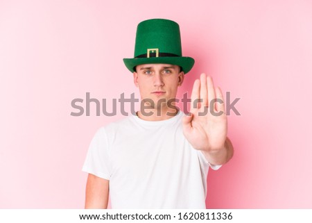 Young caucasian man celebrating saint patricks day standing with outstretched hand showing stop sign, preventing you.
