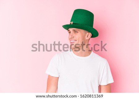 Young caucasian man celebrating saint patricks day looks aside smiling, cheerful and pleasant.