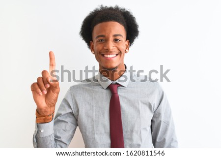 Young african american businessman wearing tie standing over isolated white background showing and pointing up with finger number one while smiling confident and happy.