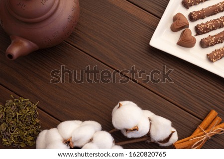 plate with chocolates on a brown wooden background with a teapot, cotton flowers, cinnamon and green tea