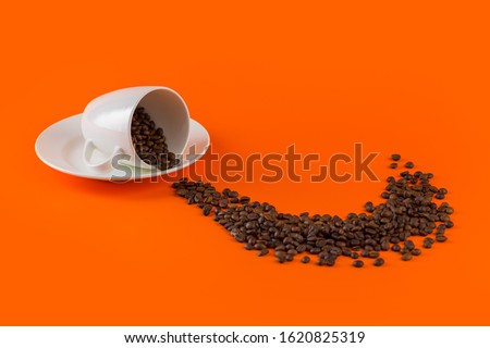 warm cup of coffee cappuccino with cream in a white cup on an orange and black background with coffee beans with a teaspoon.