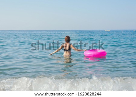 Young woman with pink swimming ring is swimming in the sea in sunny day. Summer vacation concept. Back view.